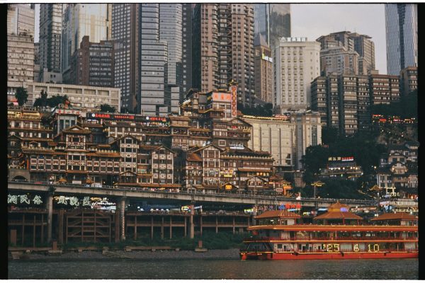 Colorful Chongqing buildings and riverboat illuminate the night, showcasing urban vibrancy.